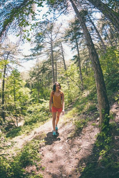 The girl is walking through the forest. A young woman with a backpack travels through picturesque places. A tourist walks along a mountain path. Fisheye lens. - Fotó, kép