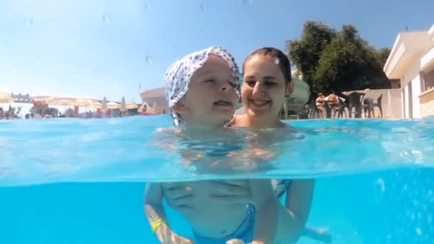 Vídeo en cámara lenta de la joven feliz sonriente con su hijo pequeño en la piscina en el complejo hotelero
 - Metraje, vídeo