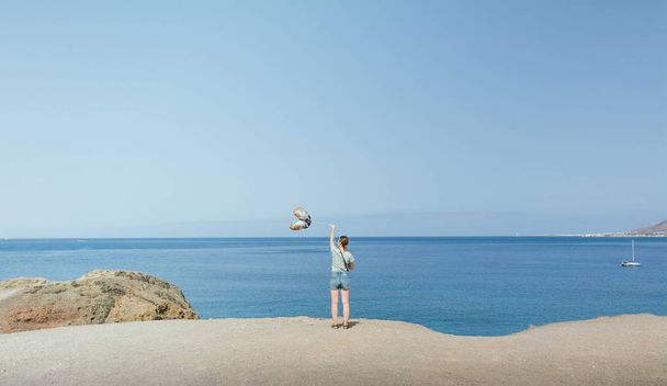 Tyttö pitää ilmapalloja meren rannalla.
 - Valokuva, kuva