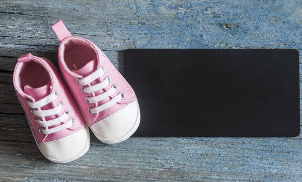トップ ビューかわいい赤ちゃん靴とあなたのテキストのための木製の背景にブラック ボード - 写真・画像