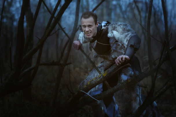 Hombre lobo con colmillos en la noche en el bosque entre los árboles
. - Foto, Imagen