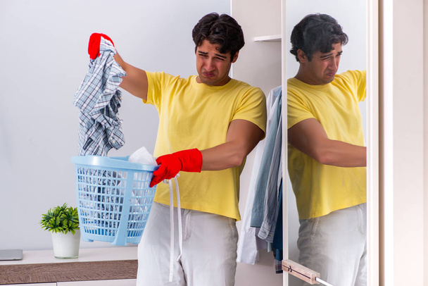 Νέος όμορφος άντρας καθαρίζει στην κρεβατοκάμαρα. - Φωτογραφία, εικόνα