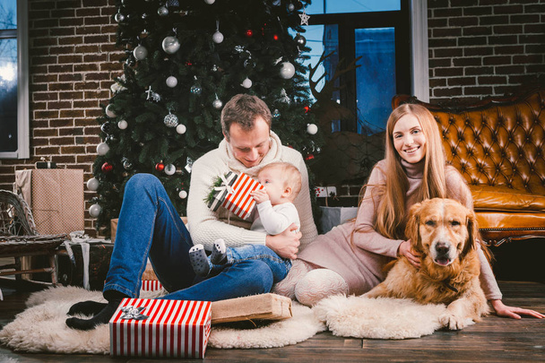 Téma karácsonyi és újévi családi körben és belföldi kisállat. Anya apa és a gyermek 1 éves kaukázusi nő ül a padló közelében karácsonyfa, ajándékok és nagy kutya fajta arany labrador Vizsla. - Fotó, kép