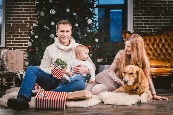 テーマ クリスマスと新年家族円と国内のペット。お母さんお父さんと子供 1 歳白人女性犬クリスマス ツリー ギフトとビッグの近くの床の上に座って繁殖黄金ラブラドル ・ レトリーバー犬. - 写真・画像