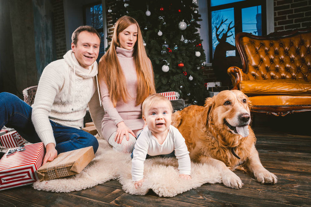 Tema Noel ve yeni yıl aile çevresi ve yerel evde beslenen hayvan. Köpek Noel ağacı hediyeler ve büyük yakın katta oturan anne baba ve çocuk 1 yaşında beyaz bir kadın doğurmak golden labrador geri almak. - Fotoğraf, Görsel