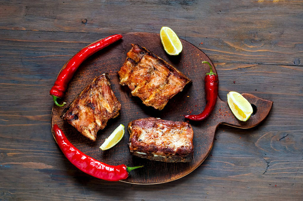 Spicy hot grilled spare ribs from BBQ served with  hot chili pepper and lime on dark wooden background.  Banner.  Top view,  copy space, flat lay. - Фото, изображение