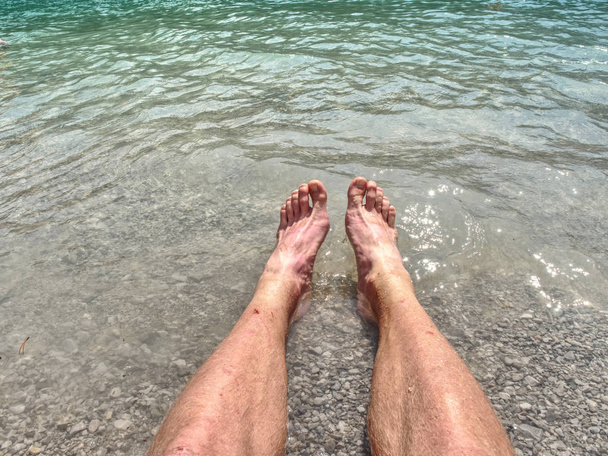 Hairy strong male legs are cooling in cold water of mountain lake. Green blue cold water of kaje in Dolomiti. - Photo, Image