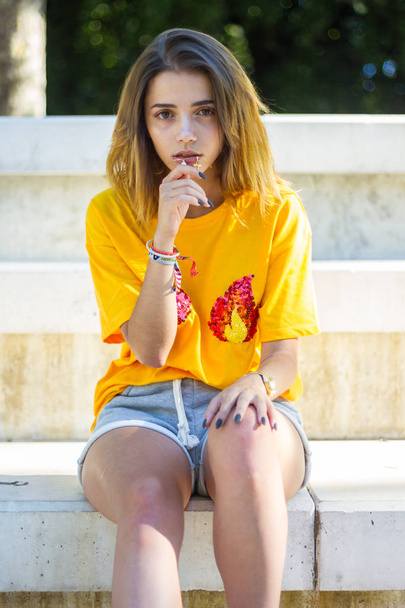 Portrait of a young woman posing on the street wearing a yellow shirt while the sun is shining.  - Photo, Image
