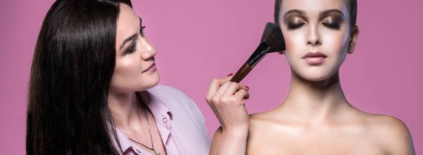 portrait of two attractive caucasian young women brunette on pink background studio shot face makeup stylst brush - Фото, зображення