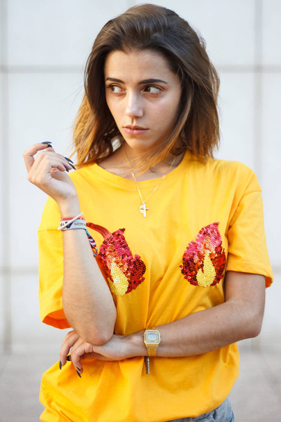 Muotokuva nuoresta naisesta poseeraamassa kadulla yllään keltainen paita, kun aurinko paistaa
.  - Valokuva, kuva