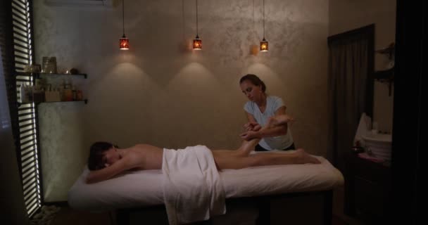 FEW SHOTS. Young woman having feet massage in beauty spa salon. Masseur kneads the foot and leg of a young beautiful girl in slow motion. - Séquence, vidéo