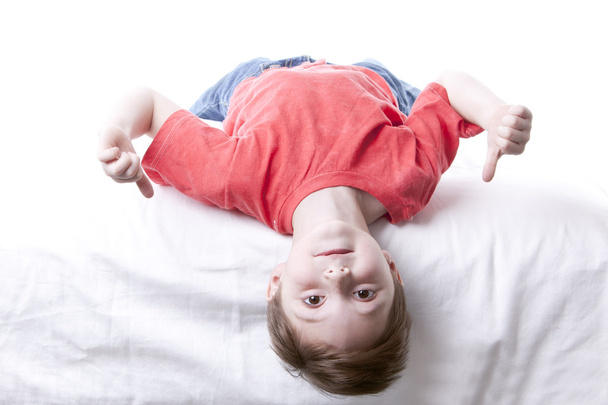 Caucasian little boy lying upside down giving the thumbs up - 写真・画像