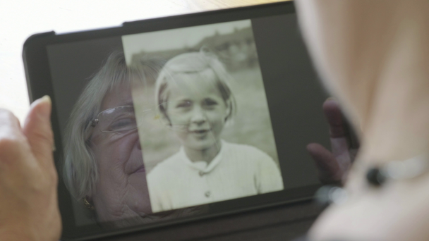 Reflection of a senior caucasian woman looking at old photos of herself on a tablet computer  - Footage, Video