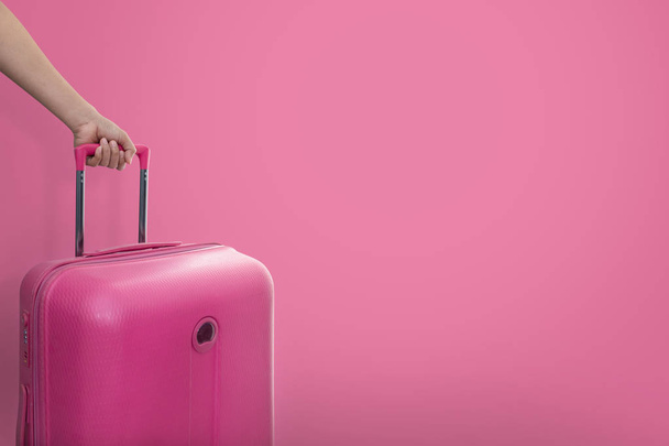 Hand holding traveler pink suitcase or cabin size luggage on pink background with copy space, Journey and travel concept. - Φωτογραφία, εικόνα