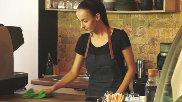 Een aantrekkelijk meisje (de eigenaar van een koffiehuis) veegt een houten tafel. - Video