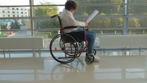 biznesmen niepełnosprawnych na wózku inwalidzkim w oknie z rysunku na dużym arkuszu papieru, omówiono pracy przez telefon - Materiał filmowy, wideo