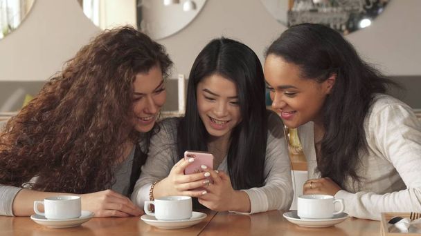 3 人の女の子はカフェでスマート フォンで何かを見る - 写真・画像