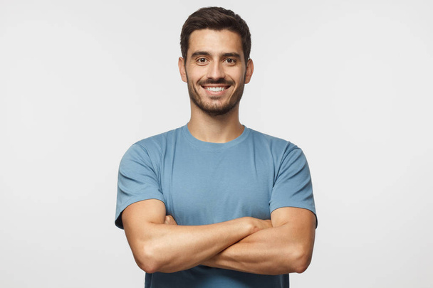 Smiling handsome man in blue t-shirt standing with crossed arms isolated on gray background - Photo, Image