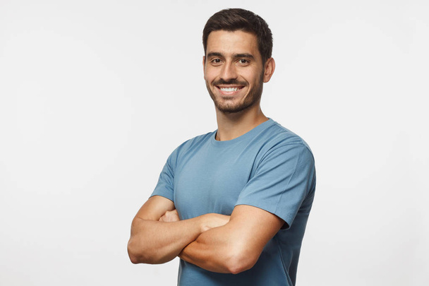 Portrait of attractive young sporty man in blue t-shirt standing with crossed arms isolated on gray background - Fotografie, Obrázek