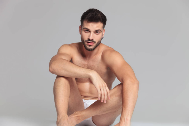 seated young man wearing only underwear is resting down on grey background - Foto, Imagem