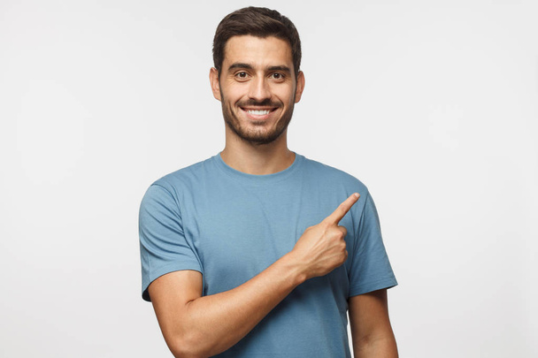 Young man in blue t-shirt pointing right with his finger isolated on gray background - Foto, imagen