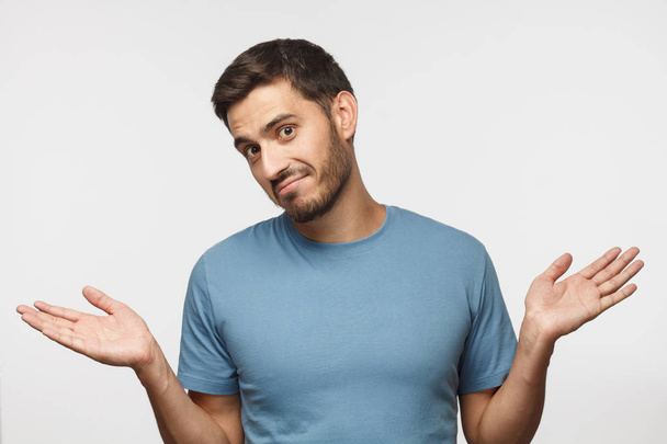 I don't know. Portrait of young confused man in blue t-shirt standing and shrugging shoulders, spreading hands isolated on gray background. I dunno - Foto, Imagem
