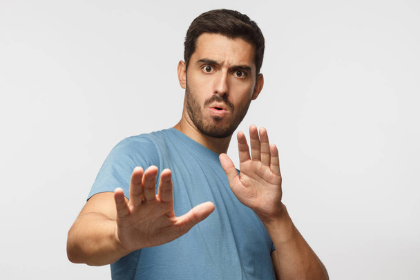 Young man showing stop gesture with both hands, wearin blue t-shirt, isolated on gray background - Fotoğraf, Görsel