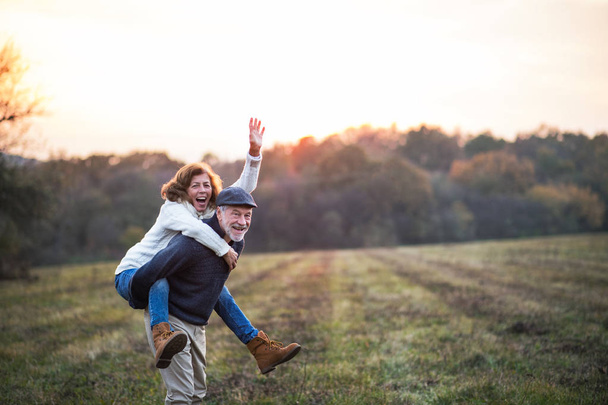 Senior man giving a woman a piggyback ride in an autumn nature. - Zdjęcie, obraz