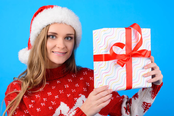 Close up portrait of charming happy smiling beautiful girl showing and holding in hands a present box, isolated on blue background
 - Фото, изображение