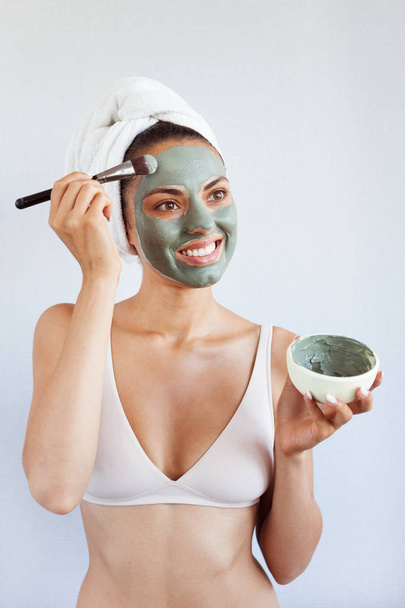 Young beautiful woman in face mask of therapeutic blue mud. Spa treatment, self care and healthy skin. Copy space, white background - Φωτογραφία, εικόνα
