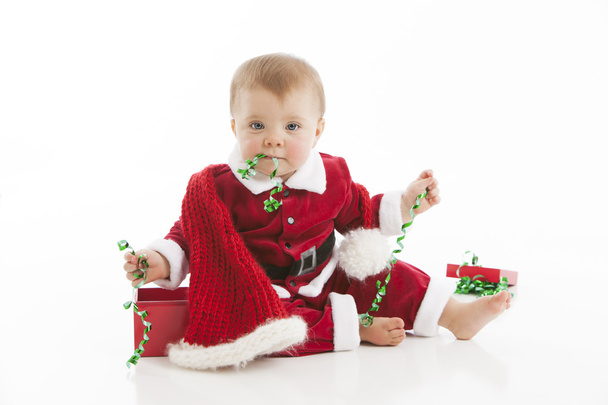Cute baby girl plays with curly christmas ribbon and puts it in her mouth - Φωτογραφία, εικόνα