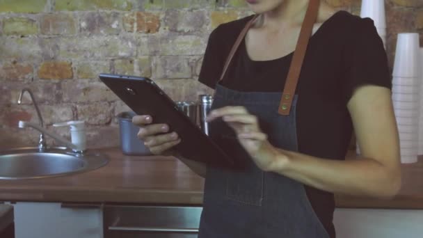 Una chica atractiva (la dueña de una cafetería) trabaja en una tableta
. - Imágenes, Vídeo