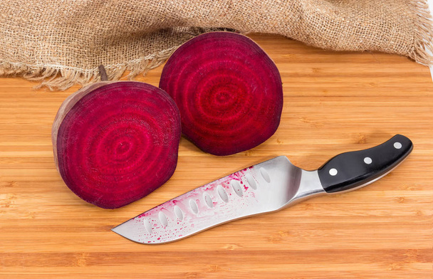 Two halves of the uncooked red beetroot cut across and kitchen knife on the bamboo wooden cutting board - Photo, Image