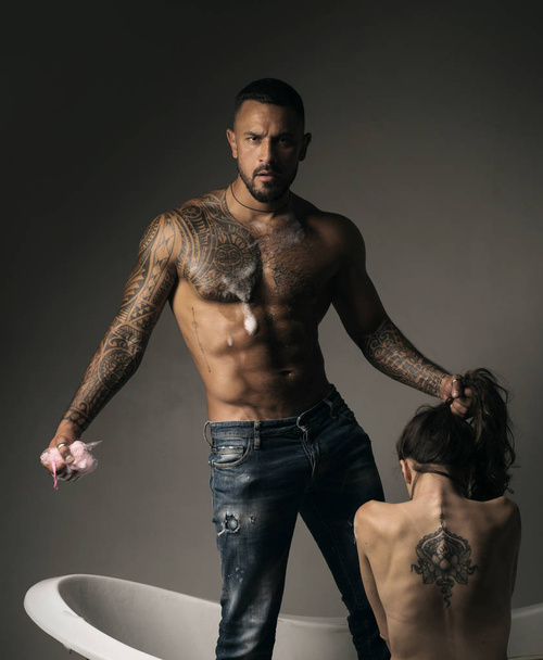 Dominantning in the foreplay sexual game. Tattooed couple. Tattooed man and woman have fun in the bathroom and he washes her beautiful back. Dominant concept. - Photo, image
