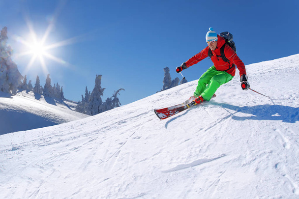 Esquiador esquiando cuesta abajo en las altas montañas contra el cielo azul
 - Foto, Imagen