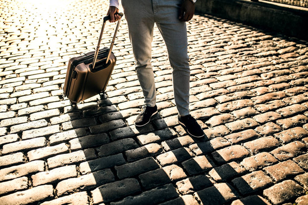 Τα πόδια του επιχειρηματία με βαλίτσα στέκεται πάνω σε ένα πεζοδρόμιο. - Φωτογραφία, εικόνα