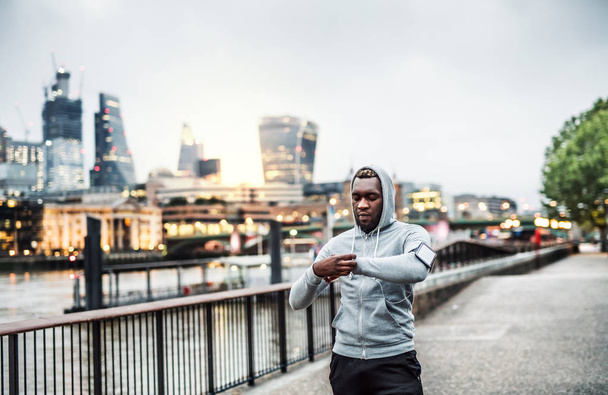 Black man runner with smartphone in an armband on the bridge in London, resting. - Фото, зображення