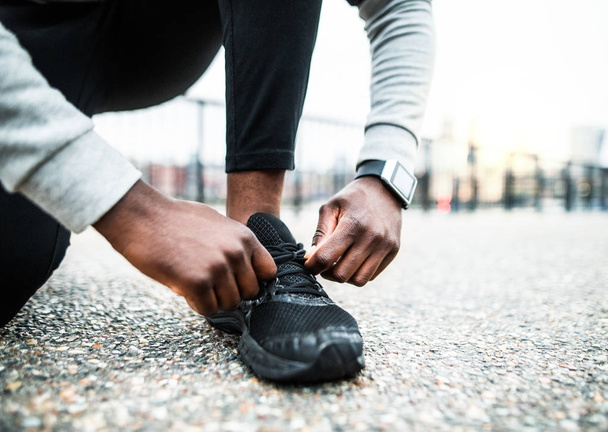 A close-up of a young sporty black man runner tying shoelaces outside in a city. - Photo, Image