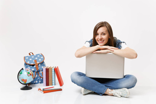 Young casual pretty smiling woman student leaning on laptop pc computer and sitting near globe backpack, school books isolated on white background. Education in high school university college concept - Photo, Image