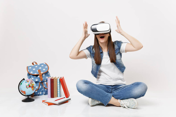 Jovem estudante surpreso usando óculos de realidade virtual estendendo as mãos desfrutando sentado perto do globo, mochila, livros escolares isolados em fundo branco. Educação na escola faculdade universitária
 - Foto, Imagem