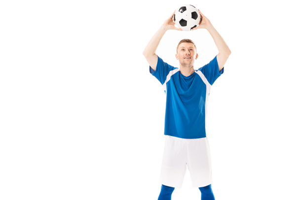 glimlachend jonge speler bedrijf voetbal boven hoofd en opzoeken van geïsoleerde op wit - Foto, afbeelding
