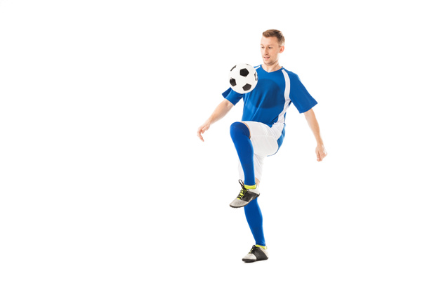 volle lengte weergave van atletische jonge sporter in uniforme opleiding van de voetbal met bal geïsoleerd op wit  - Foto, afbeelding