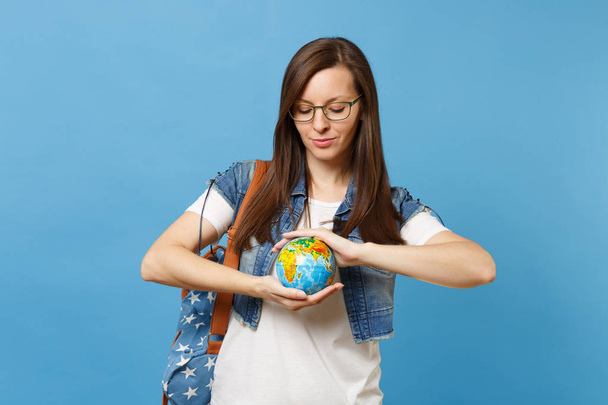 Retrato de jovem estudante mulher calma em óculos com mochila segurar olhando para baixo no globo mundial isolado em fundo azul. Educação na faculdade. Salvar planeta. Conceito de protecção ambiental ecológica
 - Foto, Imagem