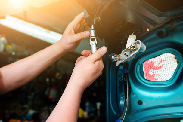 Nahaufnahme Reparatur eines kaputten blauen Autos in der Garage durch die Hände eines Mechanikers. - Foto, Bild