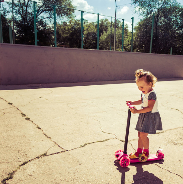 Cute child skilfully skates on a pink two-wheeled scooter on a summer sunny day - Photo, Image
