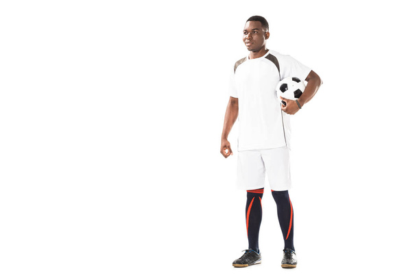 full length view of smiling young african american soccer player holding ball and looking away isolated on white - Photo, Image