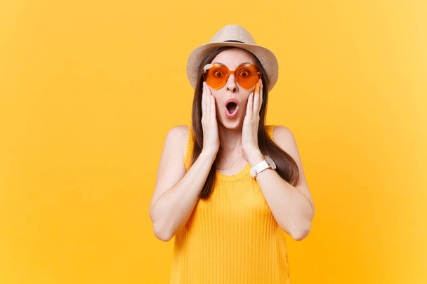 Portrait of shocked fun crazy young woman in straw summer hat, orange glasses put hands on face, copy space isolated on yellow background. People sincere emotions, lifestyle concept. Advertising area - Photo, Image