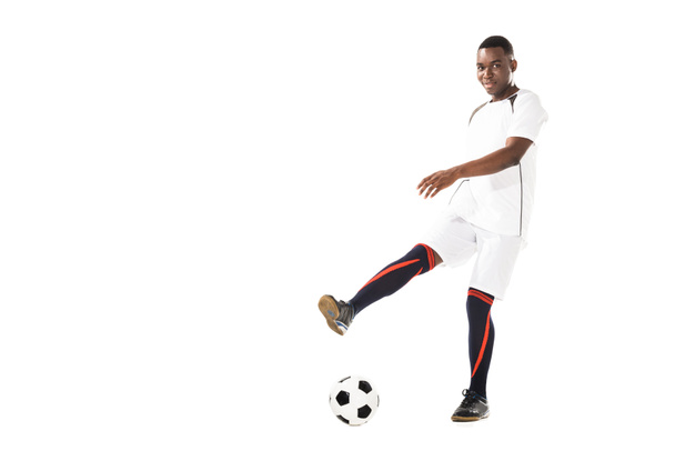 young african american soccer player kicking ball and smiling at camera isolated on white - Photo, Image