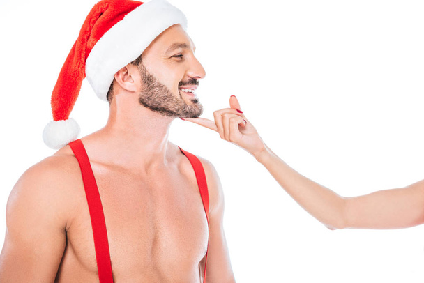 白い背景で隔離のクリスマス帽子筋肉上半身裸の彼氏のあごに触れる女性のトリミングされた画像  - 写真・画像