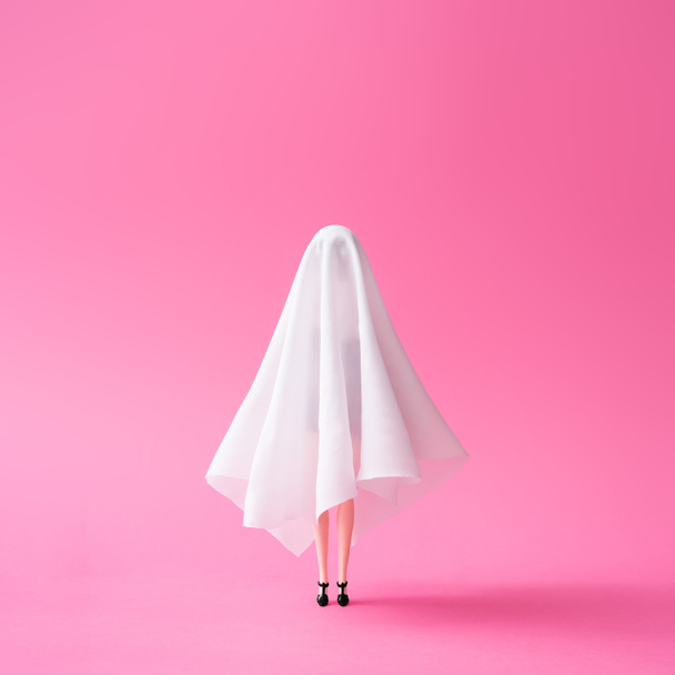 Girl doll in ghost costume against pastel pink background. Halloween party minimal concept. - Fotó, kép